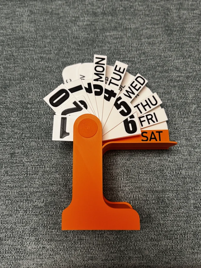 An orange printed flip-calendar stand with white date and day cards fanned open