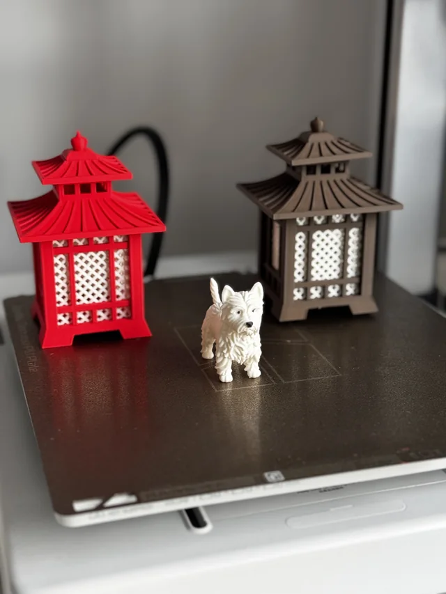 Red and brown pagoda-style printed lanterns with white patterned panels beside a small white animal figure