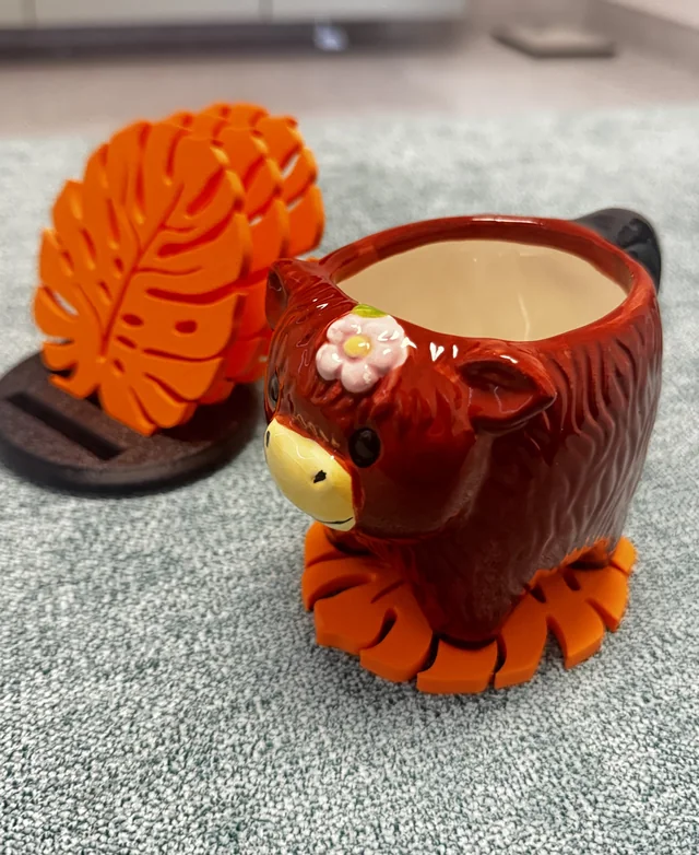 Orange leaf-shaped printed coasters, with one beneath a decorative brown mug and others standing behind it